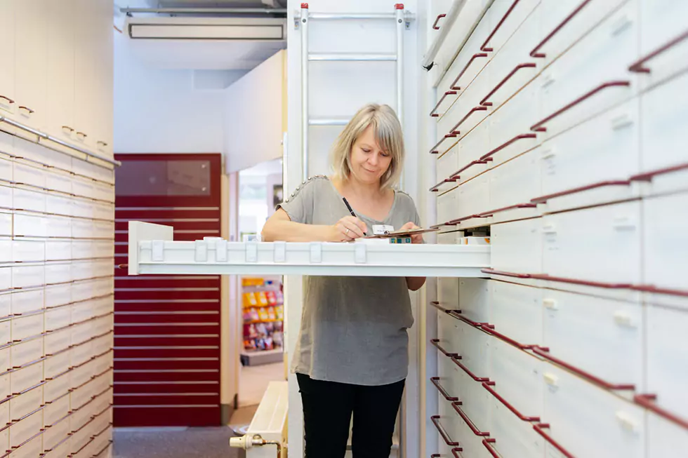 Freundliche Apothekerin schreibt eine Notiz zu Medikamenten am Apothekerschrank